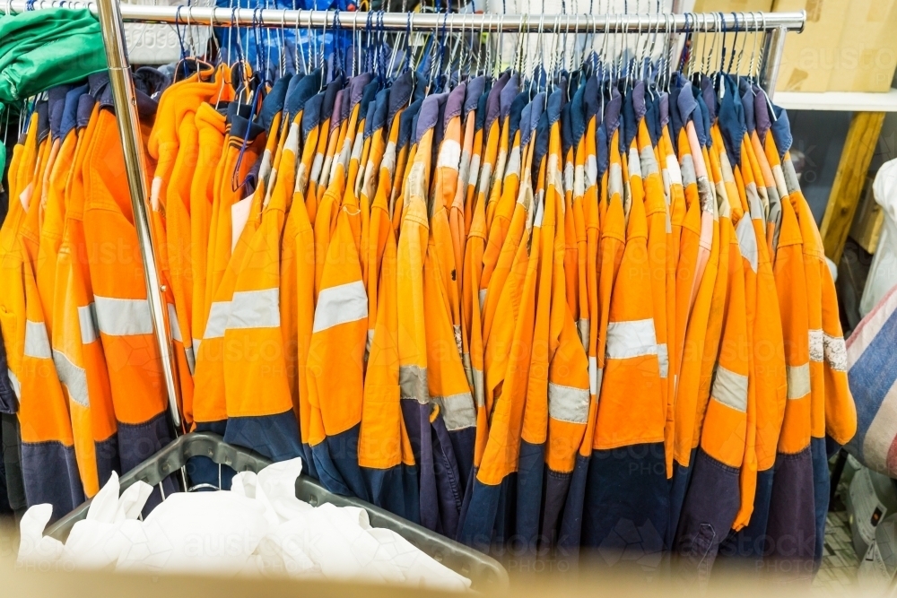 A rack full of orange hi vis work shirts hanging in a laundromat - Australian Stock Image