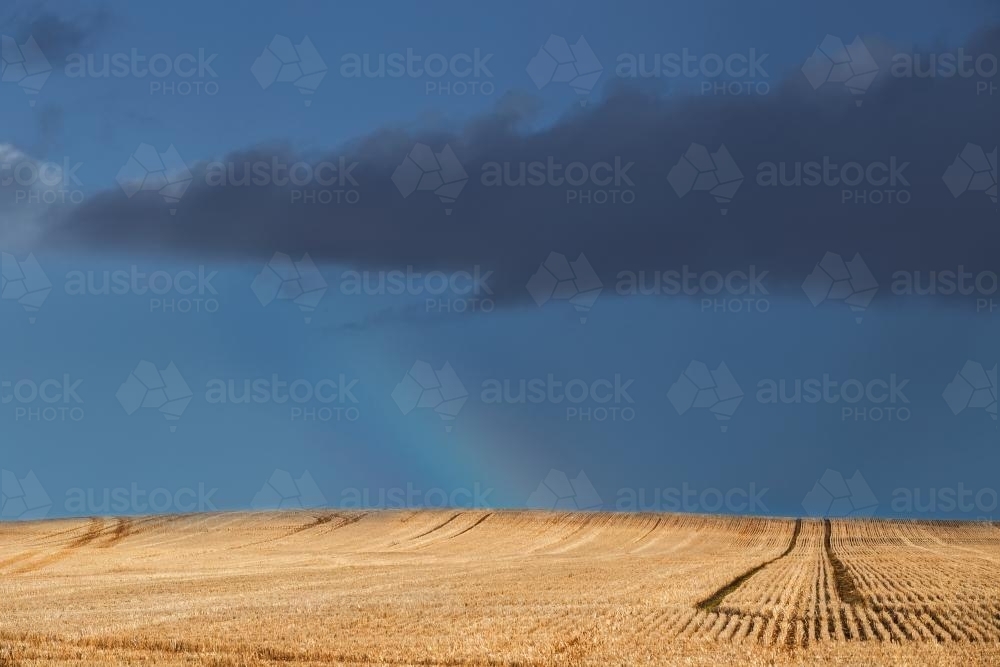 A rainbow arc and dark clouds over a paddock - Australian Stock Image