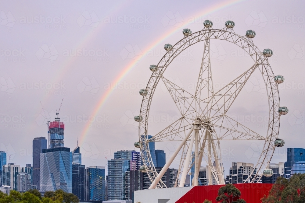 A rainbow arching over a large ferris wheel and a city skyline - Australian Stock Image