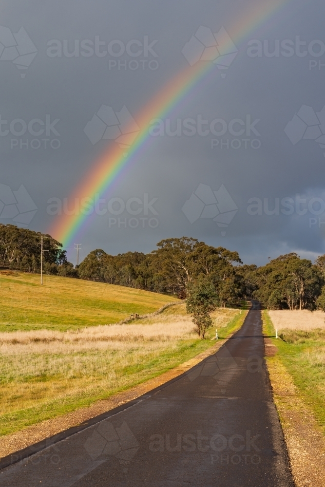A rainbow in a dark sky over a wet country road - Australian Stock Image