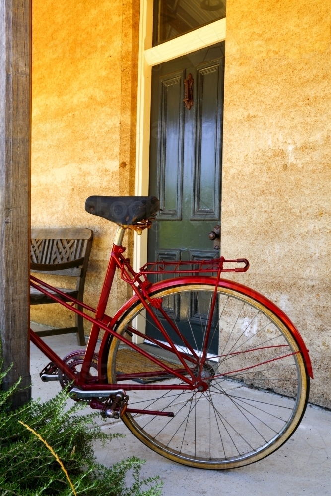 A red bicycle parked against a post outside a cottage entrance. - Australian Stock Image