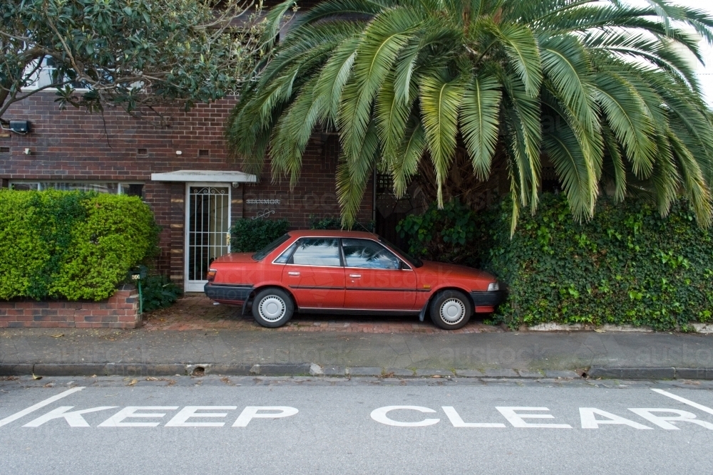A red car is parked in front of an apartment block next to a keep clear road sign - Australian Stock Image