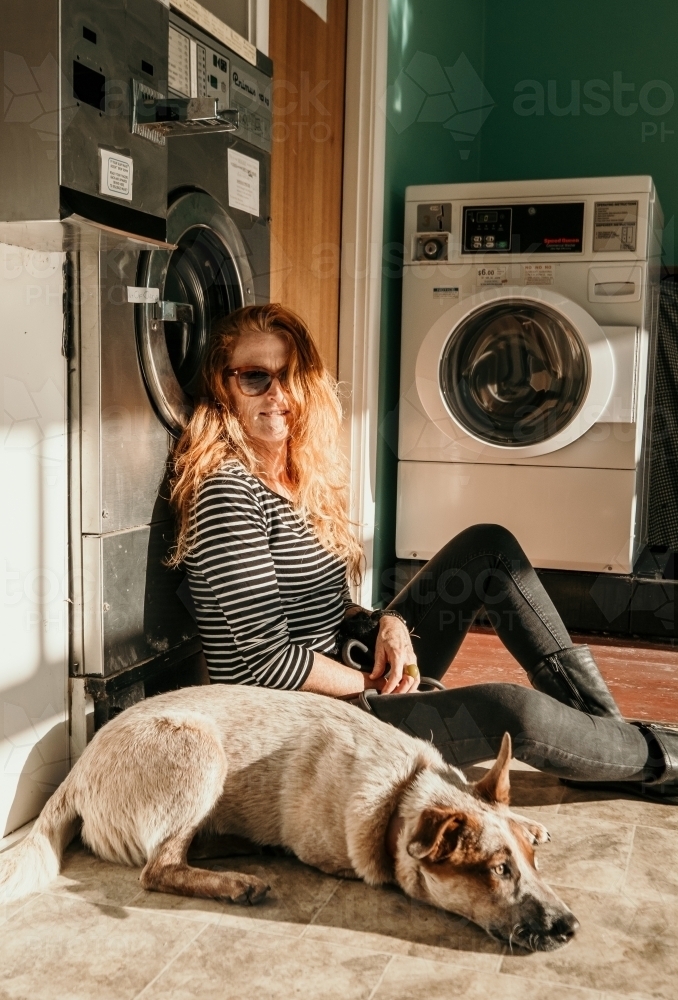 A red heeler dog sits in a laundromat with its red haired owner. - Australian Stock Image