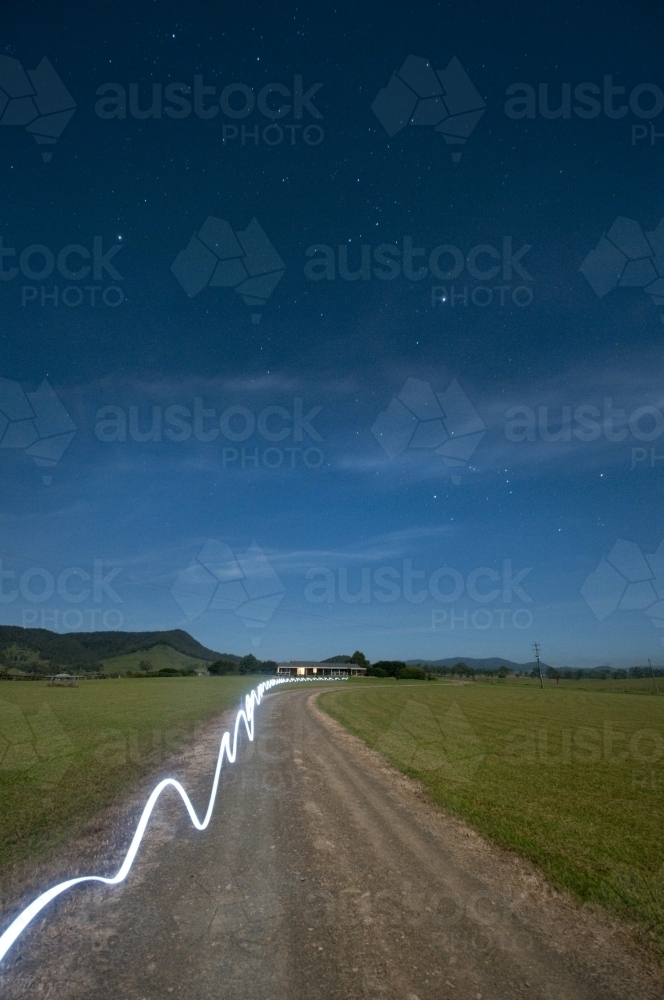 A ribbon of torchlight along a farm road at night - Australian Stock Image