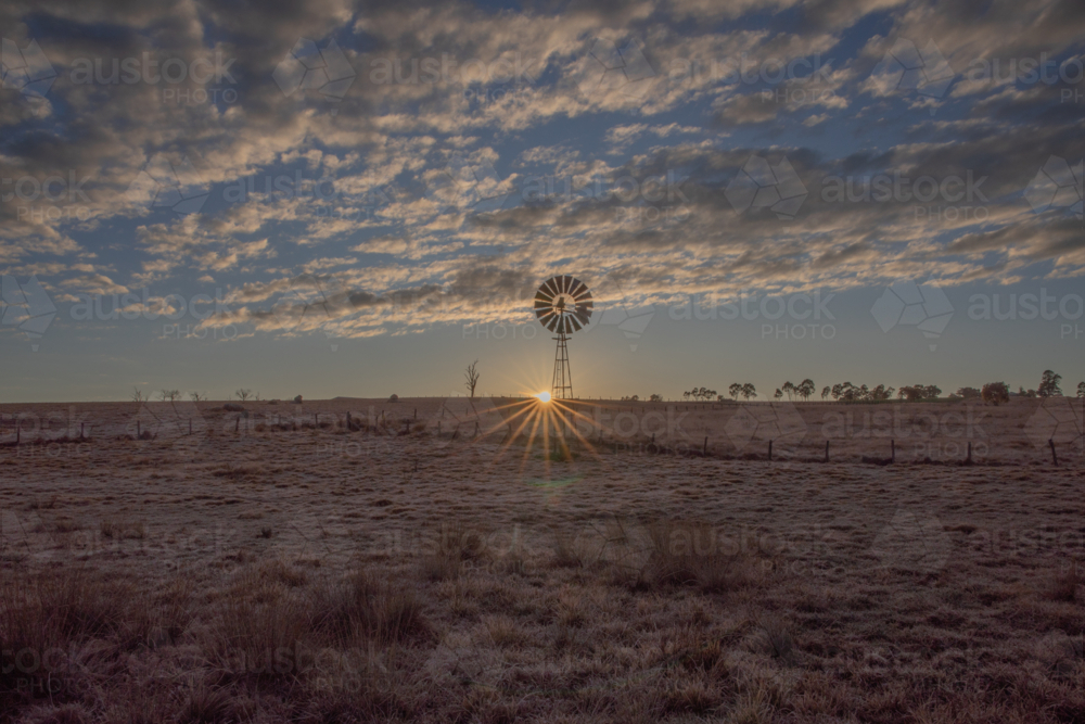 A rising sun, a country windmill and a cloudy sky - Australian Stock Image