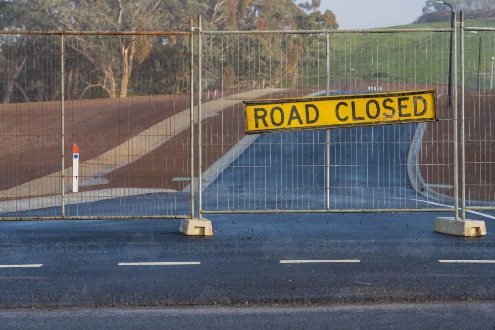 A road closed sign hanging on a fence block a brand new seal road - Australian Stock Image