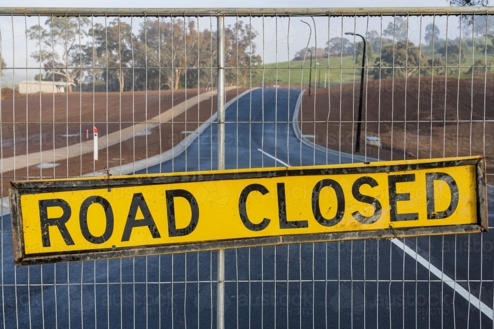 A road closed sign hanging on a fence blocking a brand new seal road - Australian Stock Image