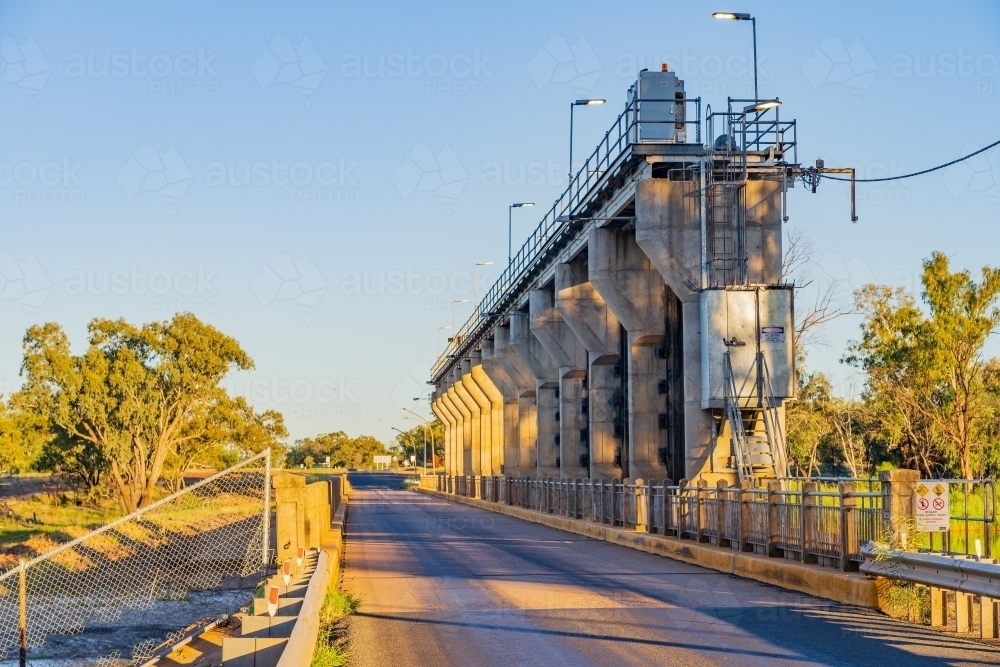 A road crossing under flood gates of a tall weir over a river - Australian Stock Image