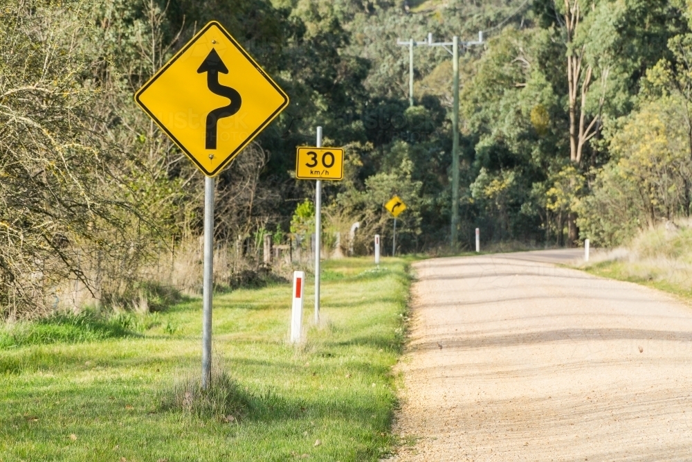 A road sign next to a country road showing an approaching bend - Australian Stock Image