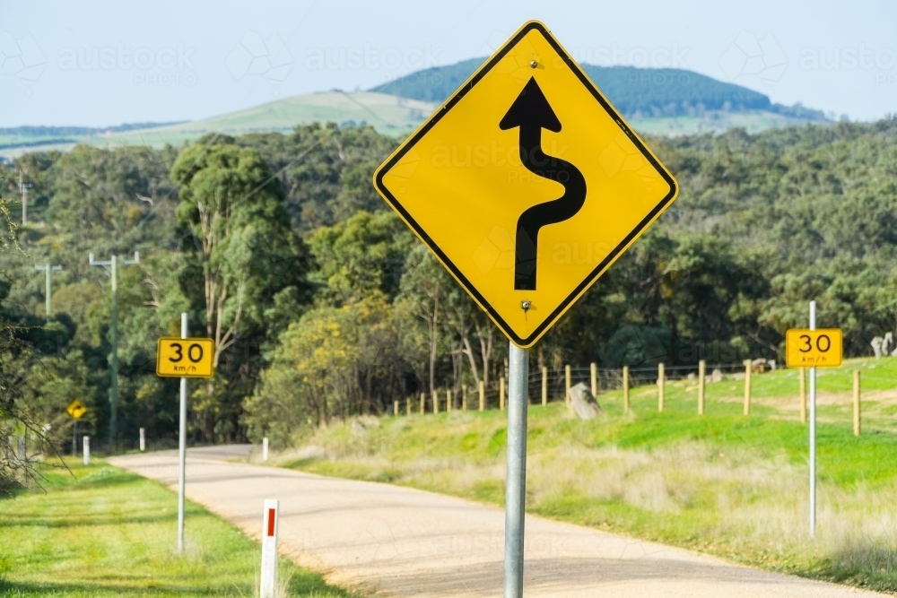 A road sign next to a country road showing an approaching bend - Australian Stock Image