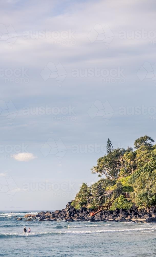 A rocky coastline, with swimmers in the foreground. - Australian Stock Image