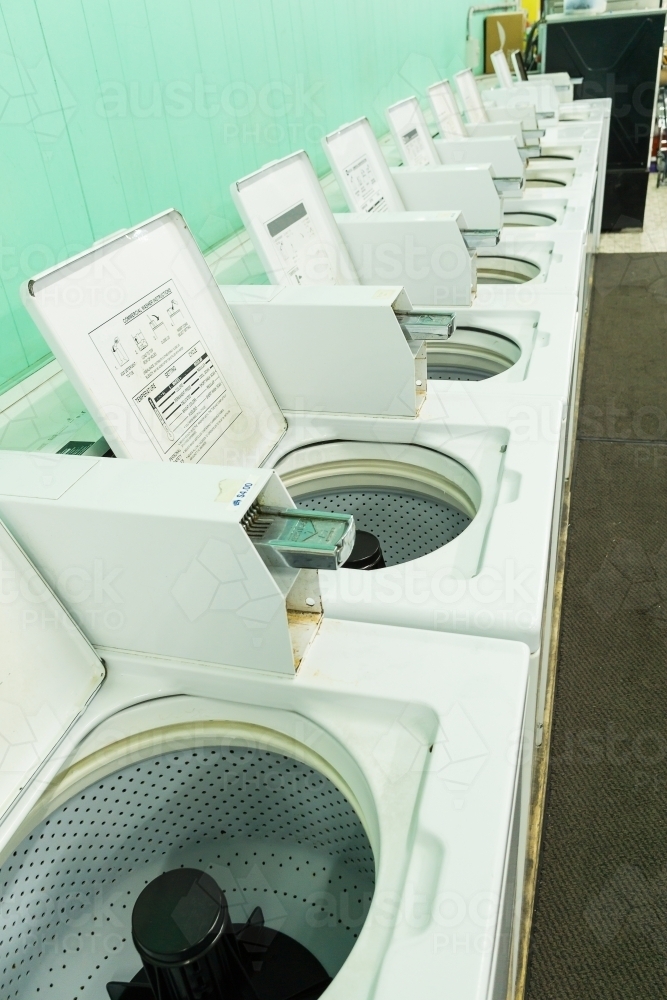 Image of A row of washing machines with their lids up in a launderette