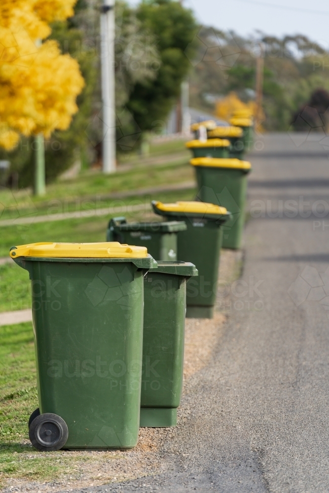 A row of wheelie bins along the side of a bitumen road - Australian Stock Image