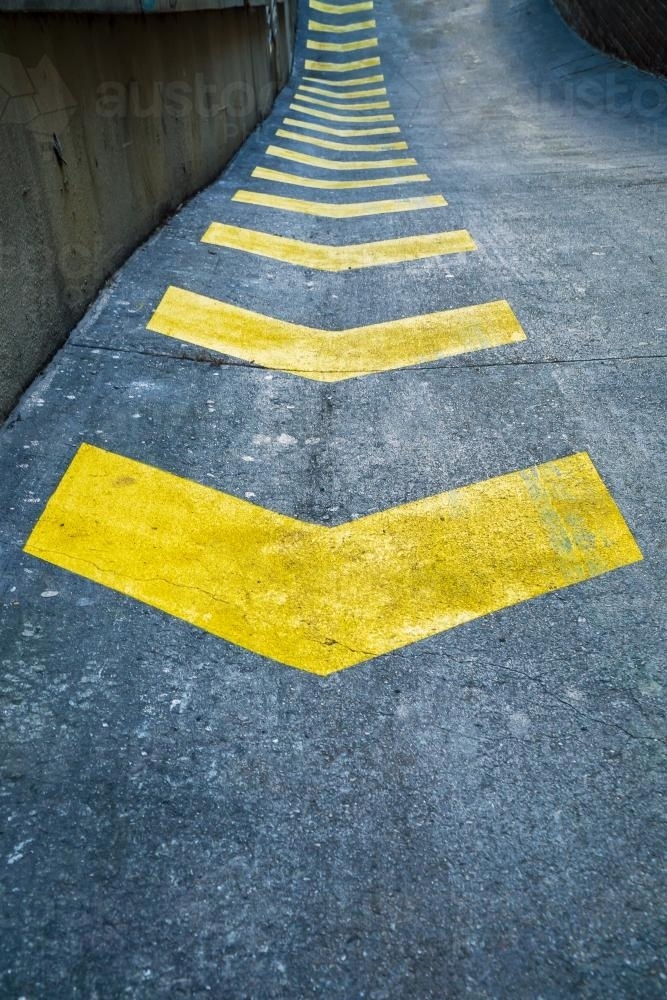 A row of yellow safety arrows painted on a road - Australian Stock Image