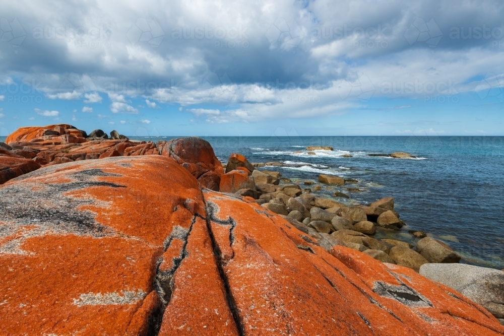 A rugged coastal scene orange, red lichen covered rocks and leading lines to a moody cloudy sky. - Australian Stock Image