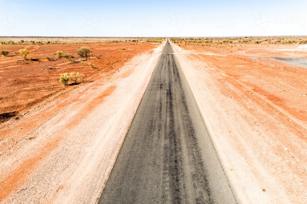 A rural highway straddled by dry red earth. - Australian Stock Image