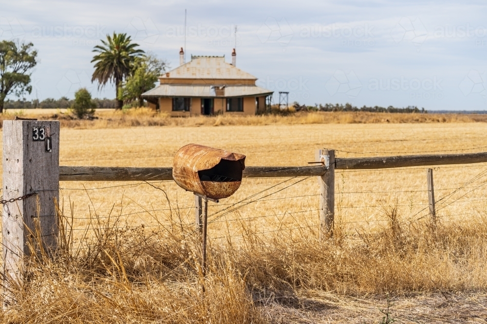 A rusted mail box in front of the fence of an old abandoned farmhouse - Australian Stock Image