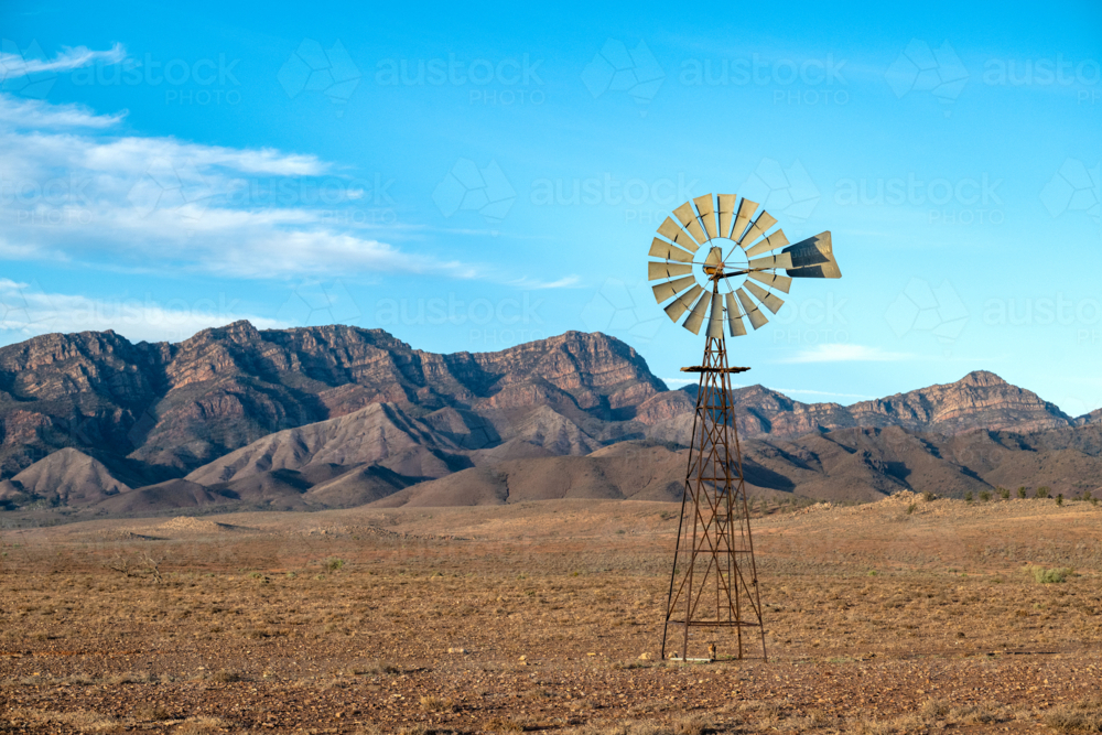 A rustic outback windmill stands before a dramatic mountain range on an arid plain - Australian Stock Image