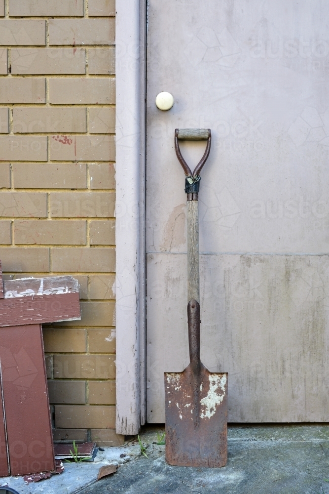 A rusty old spade leaning against a garage door - Australian Stock Image