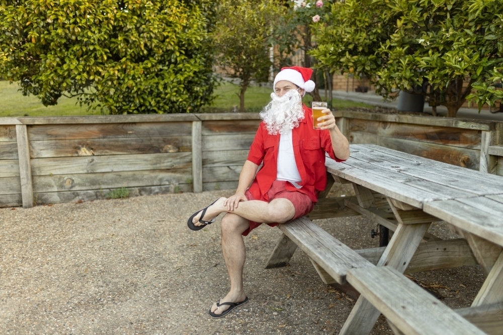 A Santa Claus at Christmas time in  the Australian summer holding a beer - Australian Stock Image