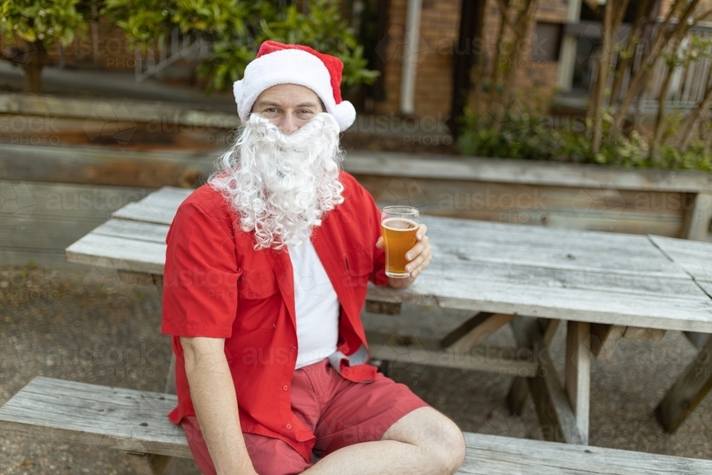 A Santa Claus at Christmas time in  the Australian summer holding a beer - Australian Stock Image
