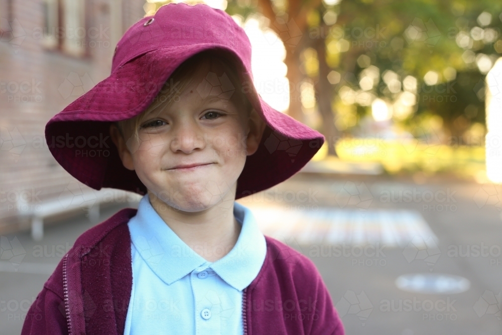 A school boy wearing his school hat grinning at the camera - Australian Stock Image