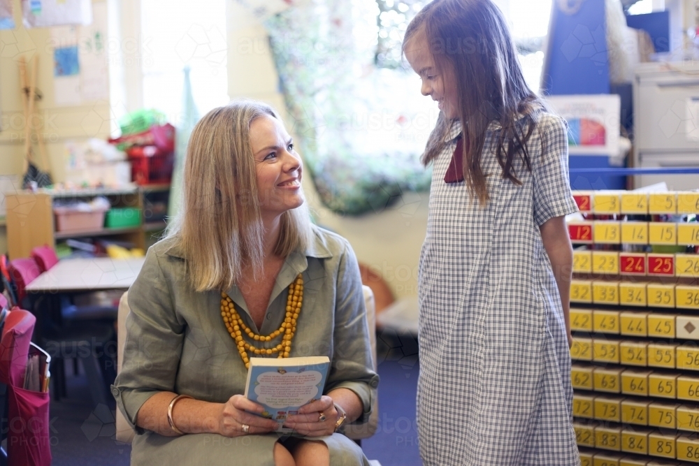 A school girl talking to her teacher in the classroom, smiling - Australian Stock Image