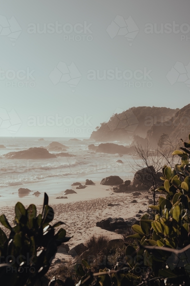 A secluded, rocky beach on a hazy morning after sunrise. - Australian Stock Image
