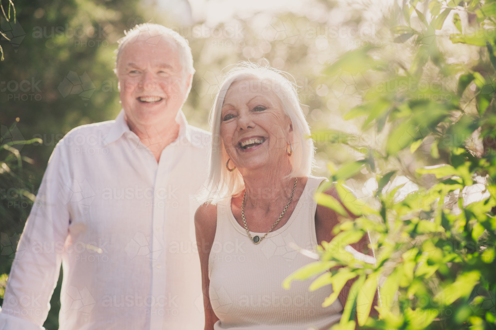 A senior couple surrounded by lush greenery and dappled sunlight - Australian Stock Image
