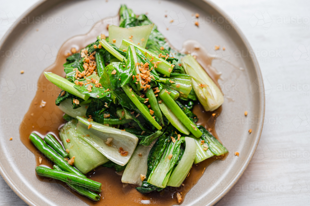 A serving of stir-fried Asian greens sits on a neutral-coloured plate - Australian Stock Image