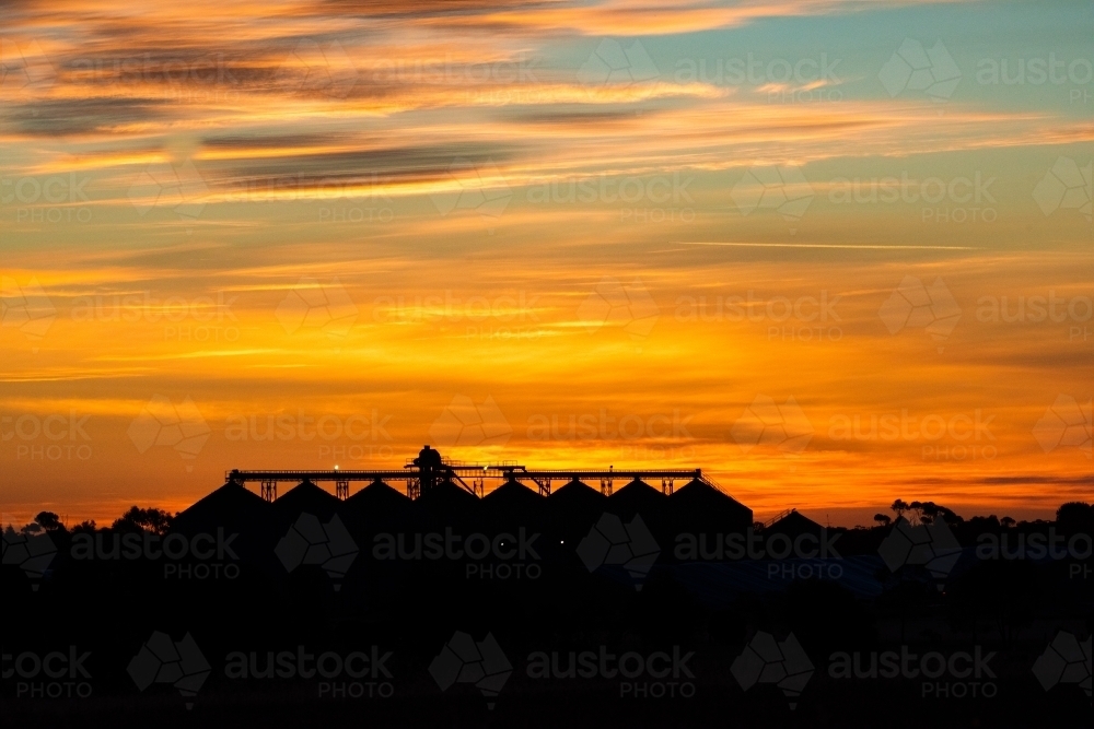 A silhouette of industrial building under the vibrant orange sunset sky with warm hues. - Australian Stock Image
