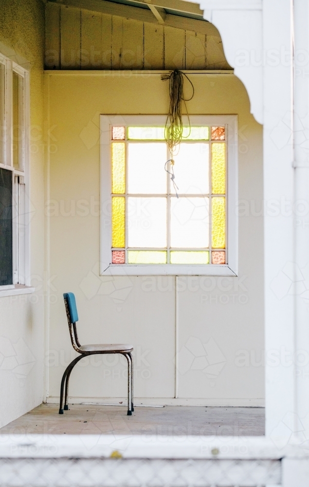 A  single chair on a country verandah with a sunlit window - Australian Stock Image
