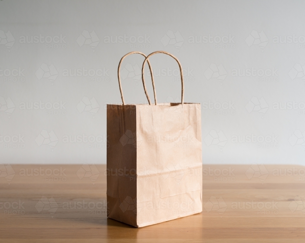A single paper bag resting on a wooden table - Australian Stock Image