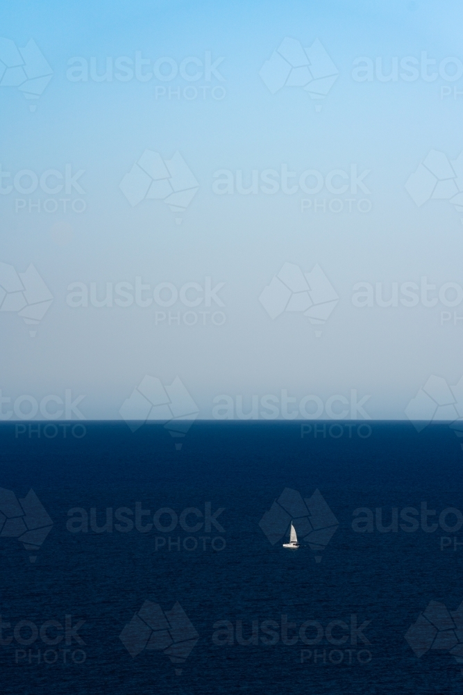 A single sailboat sailing in the middle of the deep blue ocean - Australian Stock Image