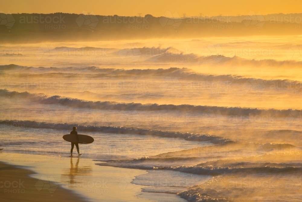 A single surfer heads into the waves at dawn - Australian Stock Image