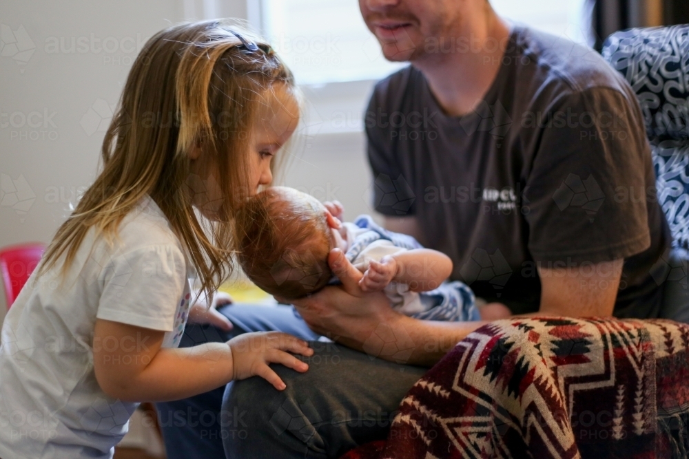 A sister kisses her newborn sibling on the forehead - Australian Stock Image
