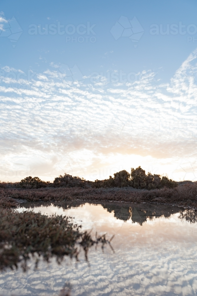 A sky with scattered clouds and warm glow of the sun reflecting on the water - Australian Stock Image
