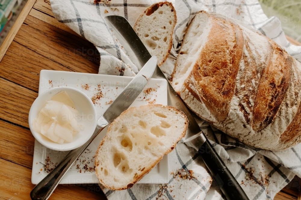 A slice of bread on a white plate with butter with Home made Sour dough bread cooling on a tea towel - Australian Stock Image