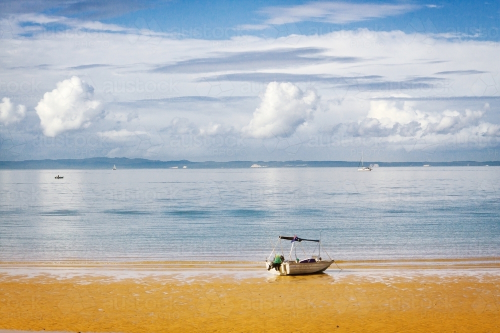 A small boat sitting on the edge of a sandy beach with puffy clouds in the sky above - Australian Stock Image