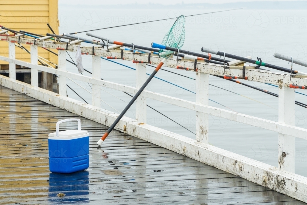 Image of A small esky sitting on a jetty next to a row of fishing rods attached to the railing