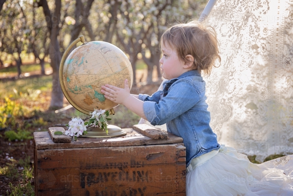A Small Girl Holding a World Globe in a Flower Orchard - Australian Stock Image