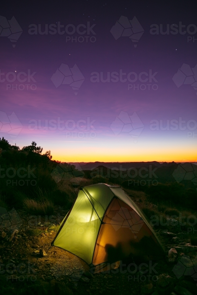 A small two person tent illuminated from a camper inside the tent at night. - Australian Stock Image
