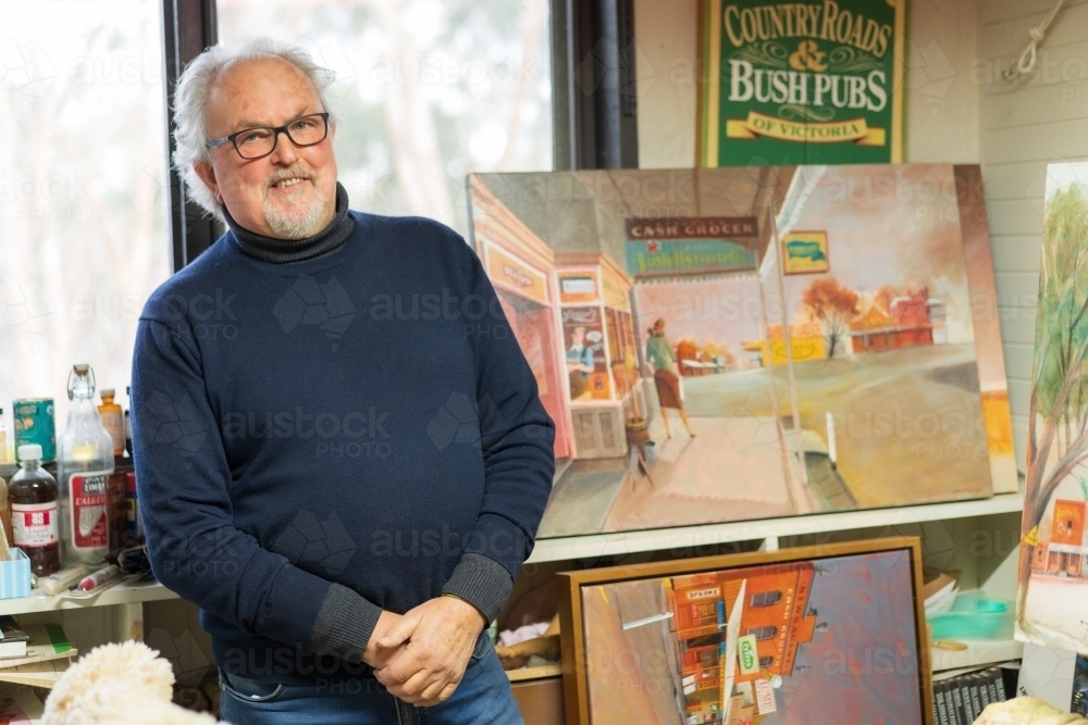 A smiling male artist standing by his paintings in an art studio - Australian Stock Image