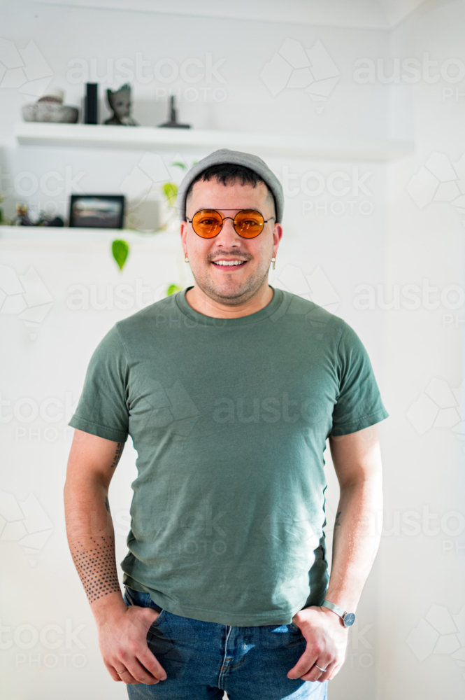 A smiling man in his 30s wears sunglasses and a T-shirt in a bright room. - Australian Stock Image