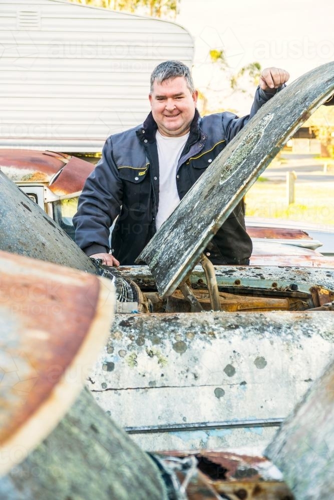 A smiling man stands by an old car leaning on its bonnet - Australian Stock Image