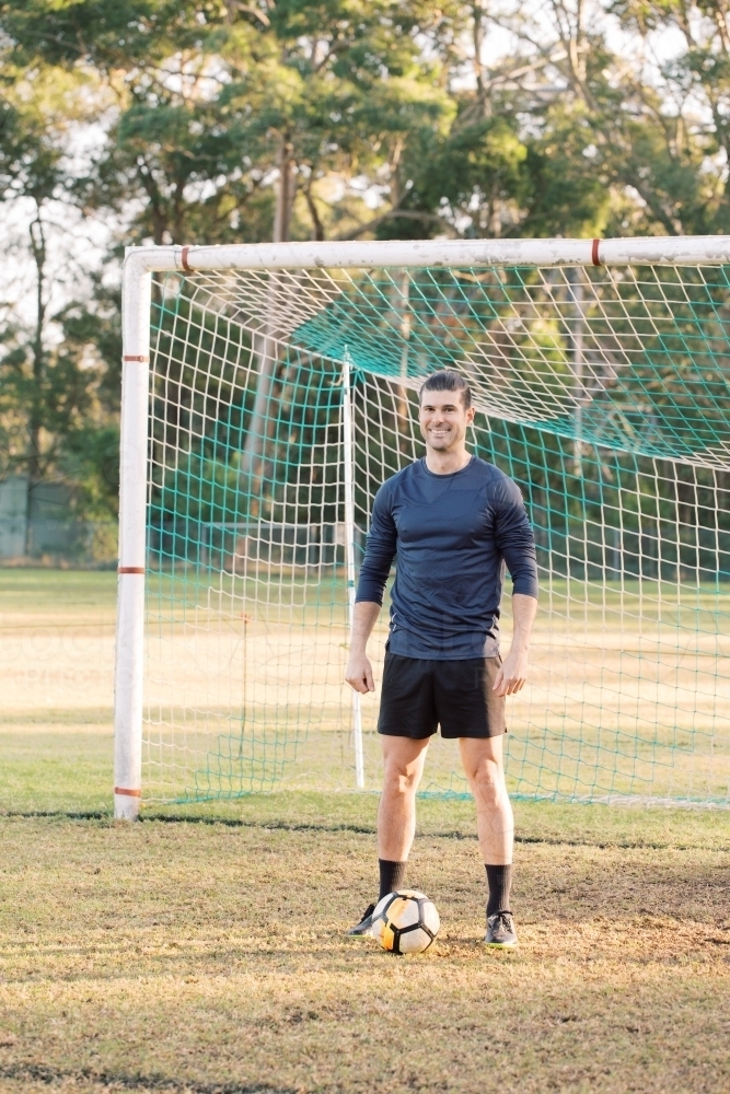a smiling young man standing on the field with a soccer ball in front of him - Australian Stock Image