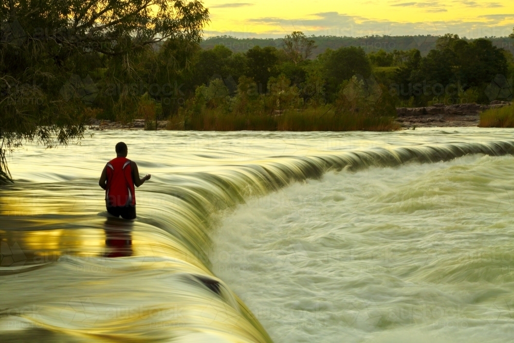 A solitary man uses a hand line fishing for barramundi at Ivanhoe Crossing on the Ord River. - Australian Stock Image