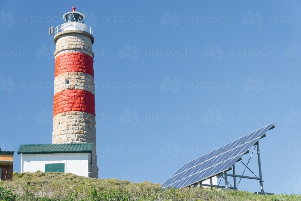 A stone lighthouse on a hill next to an array of solar panels - Australian Stock Image