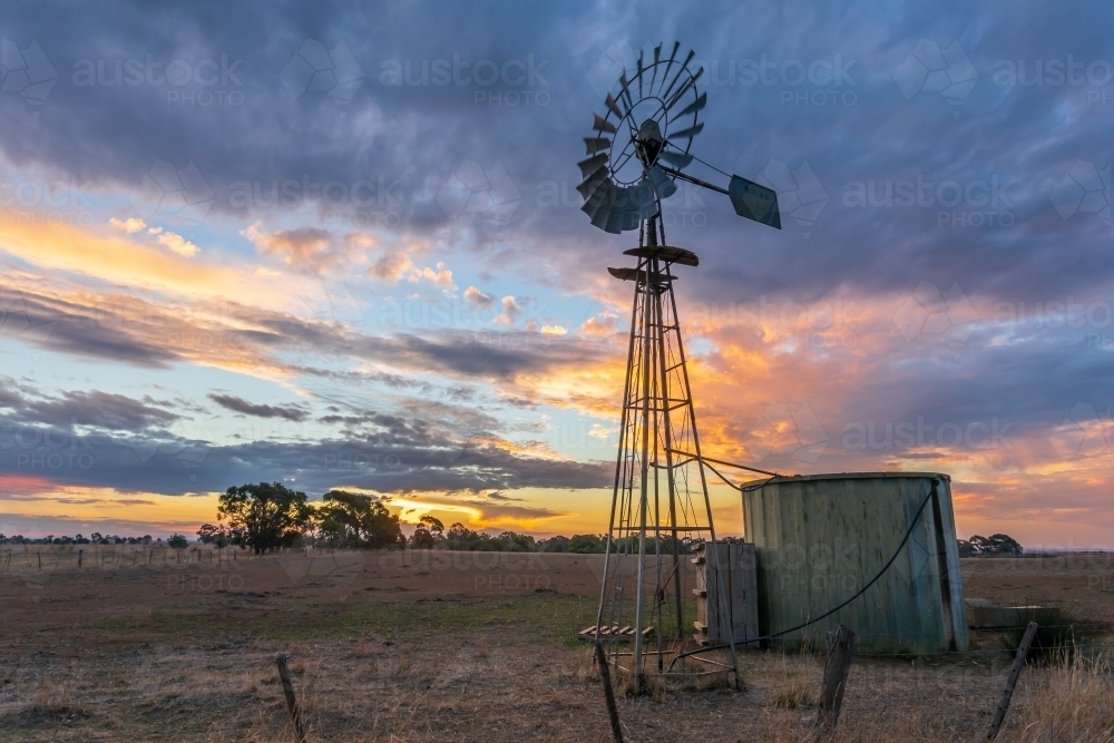 A sunset behind a  windmill and water tank on farmland - Australian Stock Image