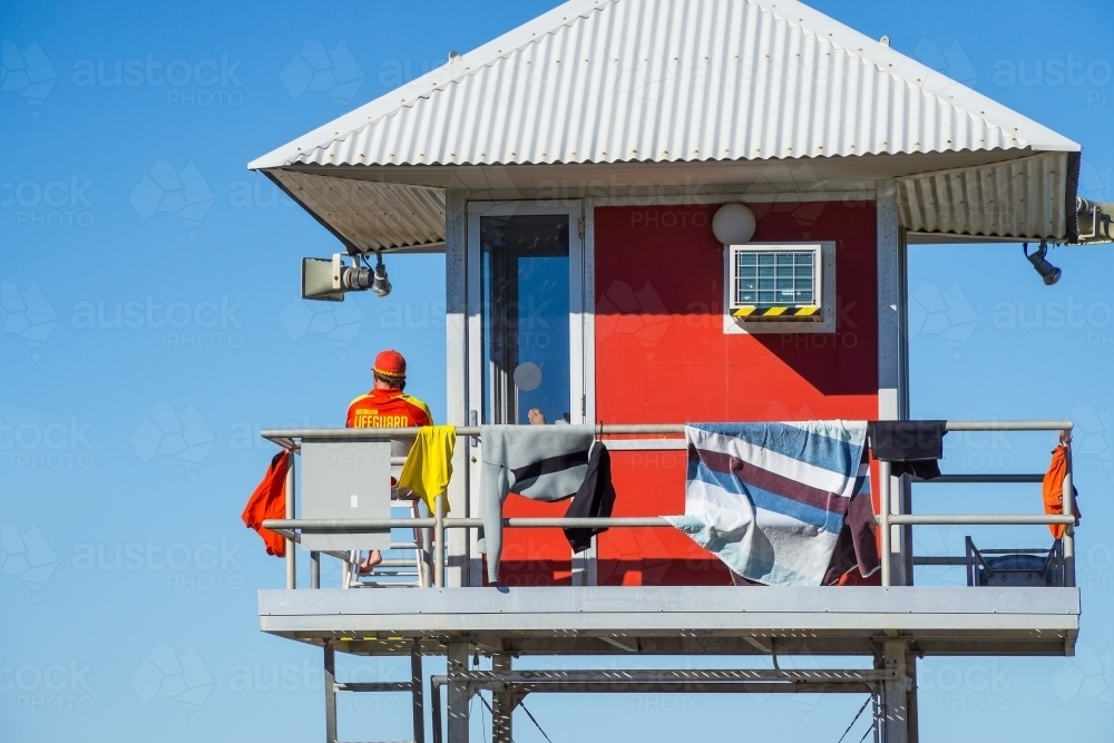 A surf lifeguard sitting in a watch tower with a corrugated tin roof. - Australian Stock Image